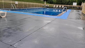 Piscina com borda azul, escada de metal e área cercada com cadeiras e guarda-sóis.