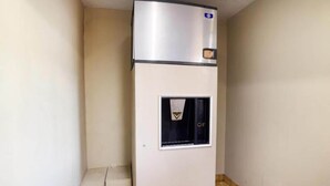 Uma geladeira compacta com compartimento para congelador, situada num canto de um quarto com piso de azulejos e paredes lisas.