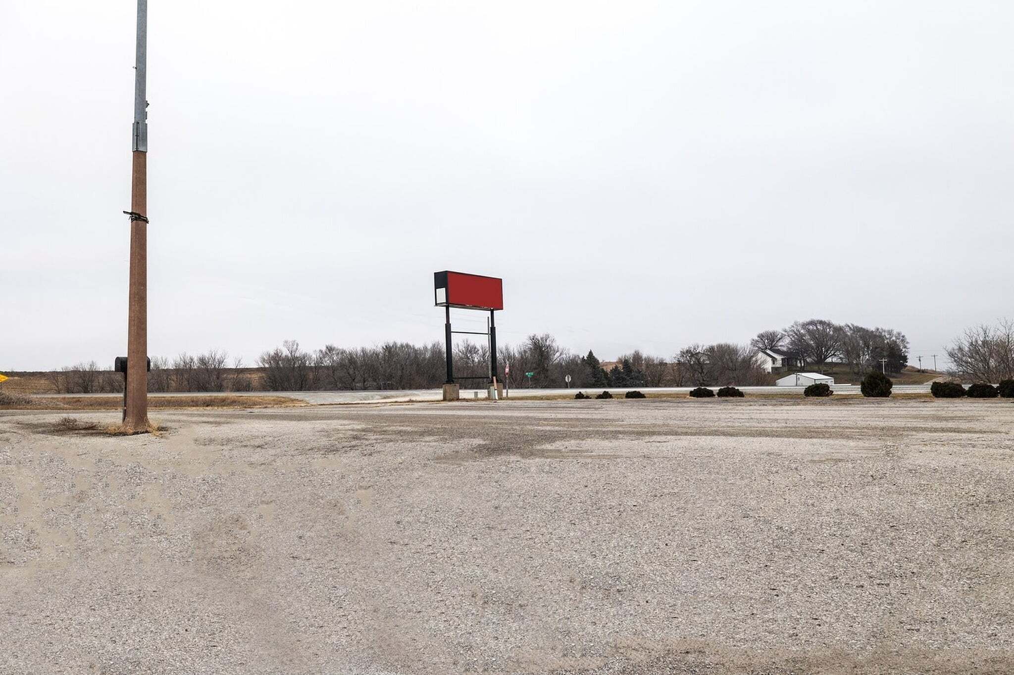 A gravel parking lot with a red billboard, a utility pole, and sparse vegetation.