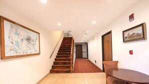 Un couloir avec un escalier en bois, un coin repas avec une table et des chaises, et une carte encadrée accrochée au mur.
