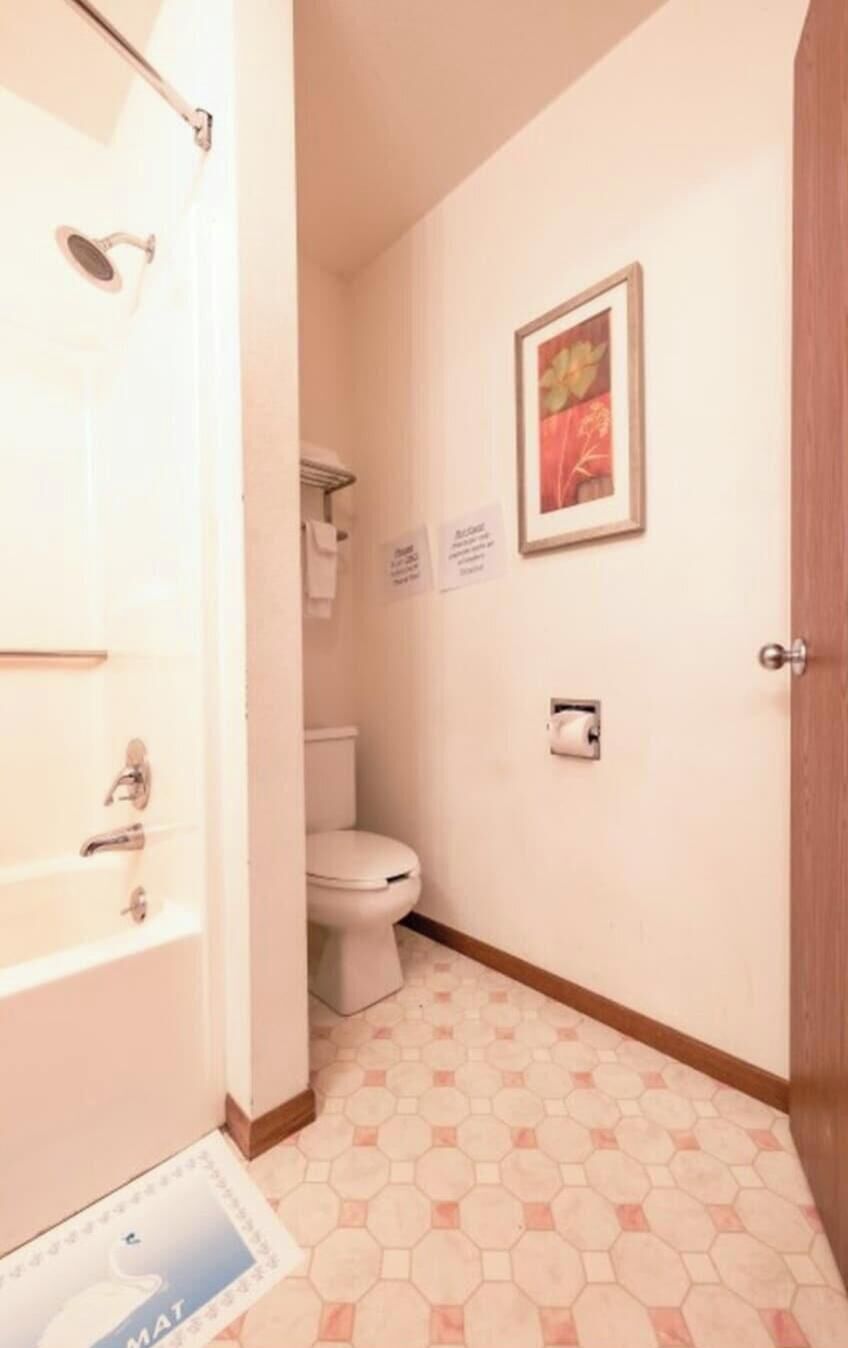 Un pasillo estrecho con ducha, inodoro y una puerta que da a otra habitación.