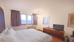 Une chambre d’hôtel avec un lit, un téléviseur posé sur une commode en bois, une fenêtre avec des rideaux et une petite poubelle.