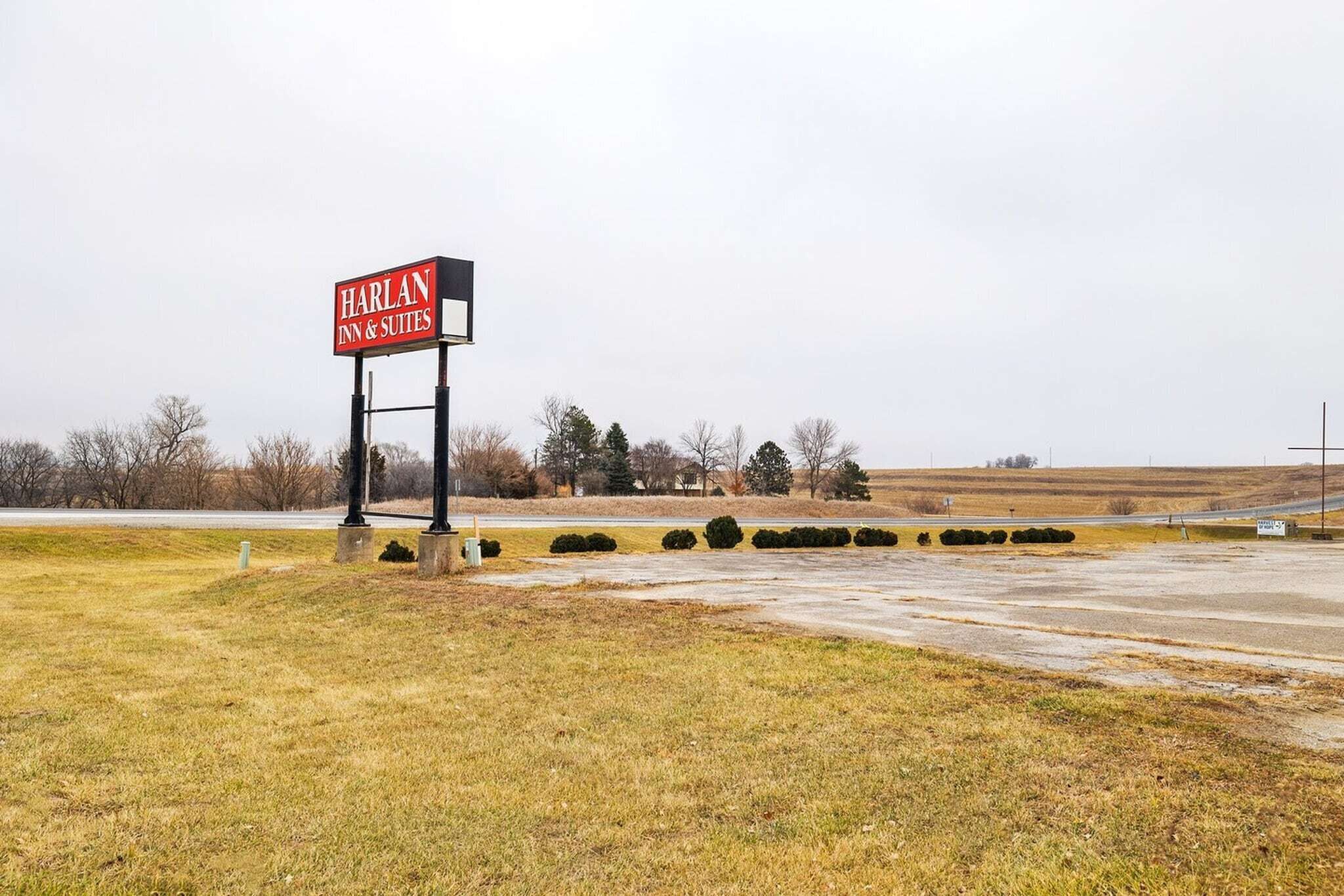 A sign for Harlan Inn & Suites in a rural setting with open fields and sparse trees.