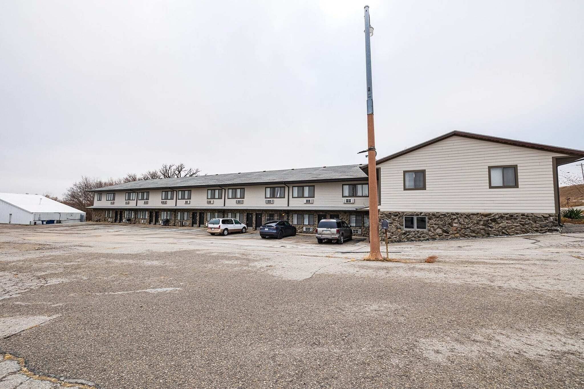 Un motel avec une rangée de chambres, un parking et un poteau électrique élevé.