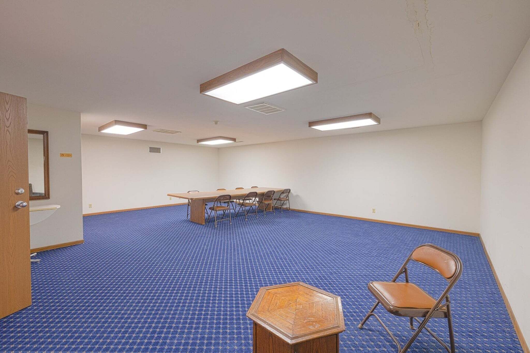 A conference room with a long table, chairs, a hexagonal table, and a folding chair.