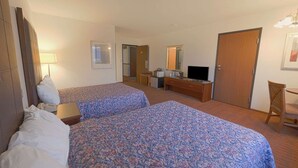 Quarto de hotel com duas camas, uma escrivaninha, televisão, guarda-roupa e espelho.