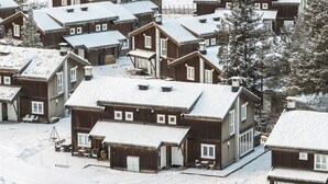 Eine Gruppe Holzhäuser mit schneebedeckten Dächern unter blauem Himmel.
