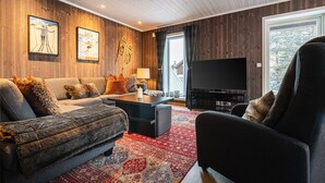 Ein gemütliches Wohnzimmer mit Sofa, Sesseln, Fernseher und einem gemusterten Teppich.