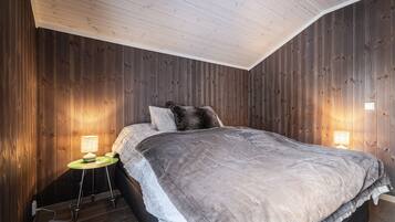 A bedroom with a wooden wall, a bed with a grey blanket, and two bedside lamps.