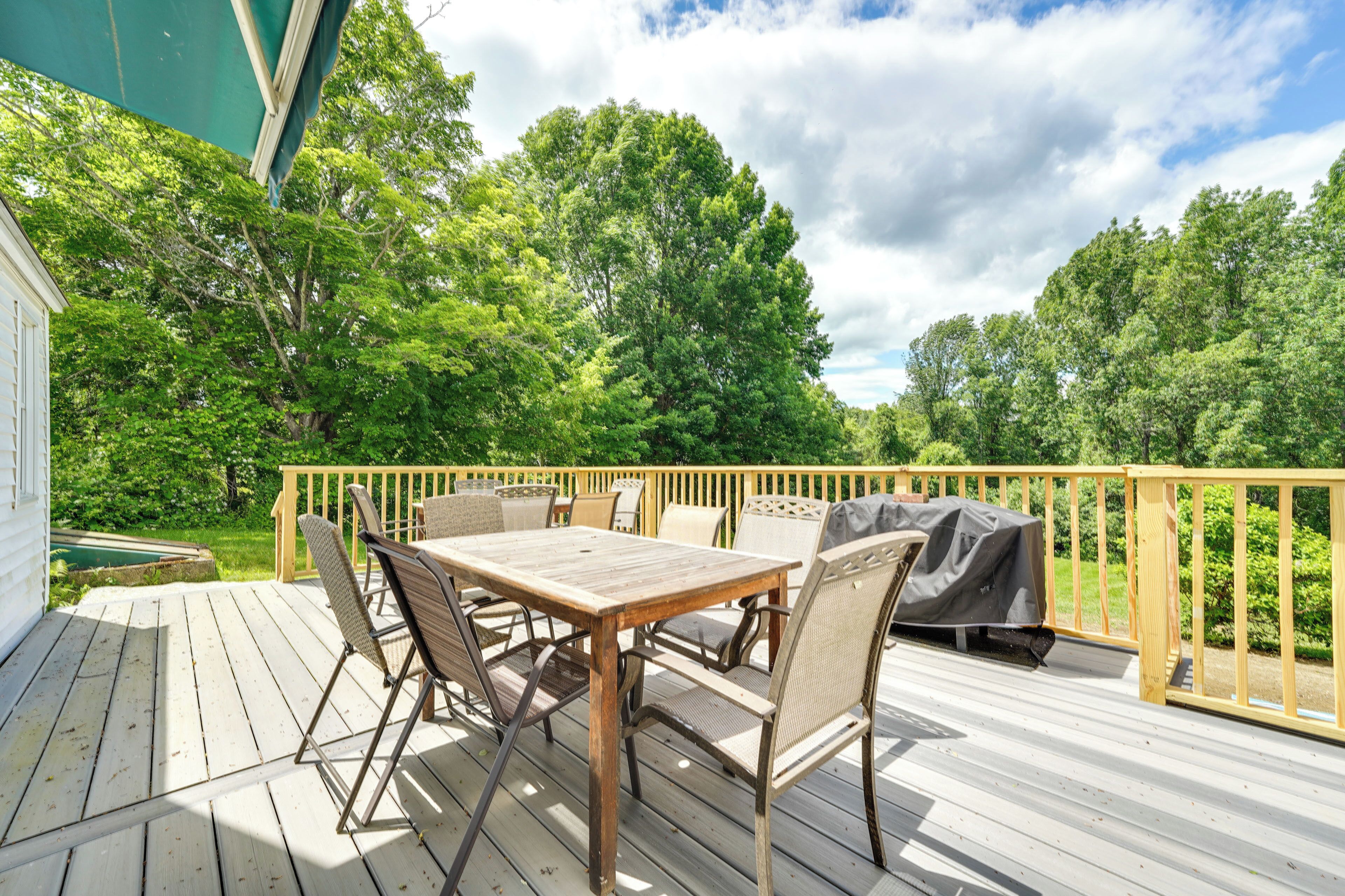 Une terrasse en bois avec une table et des chaises, un barbecue et une vue sur les arbres et une maison.