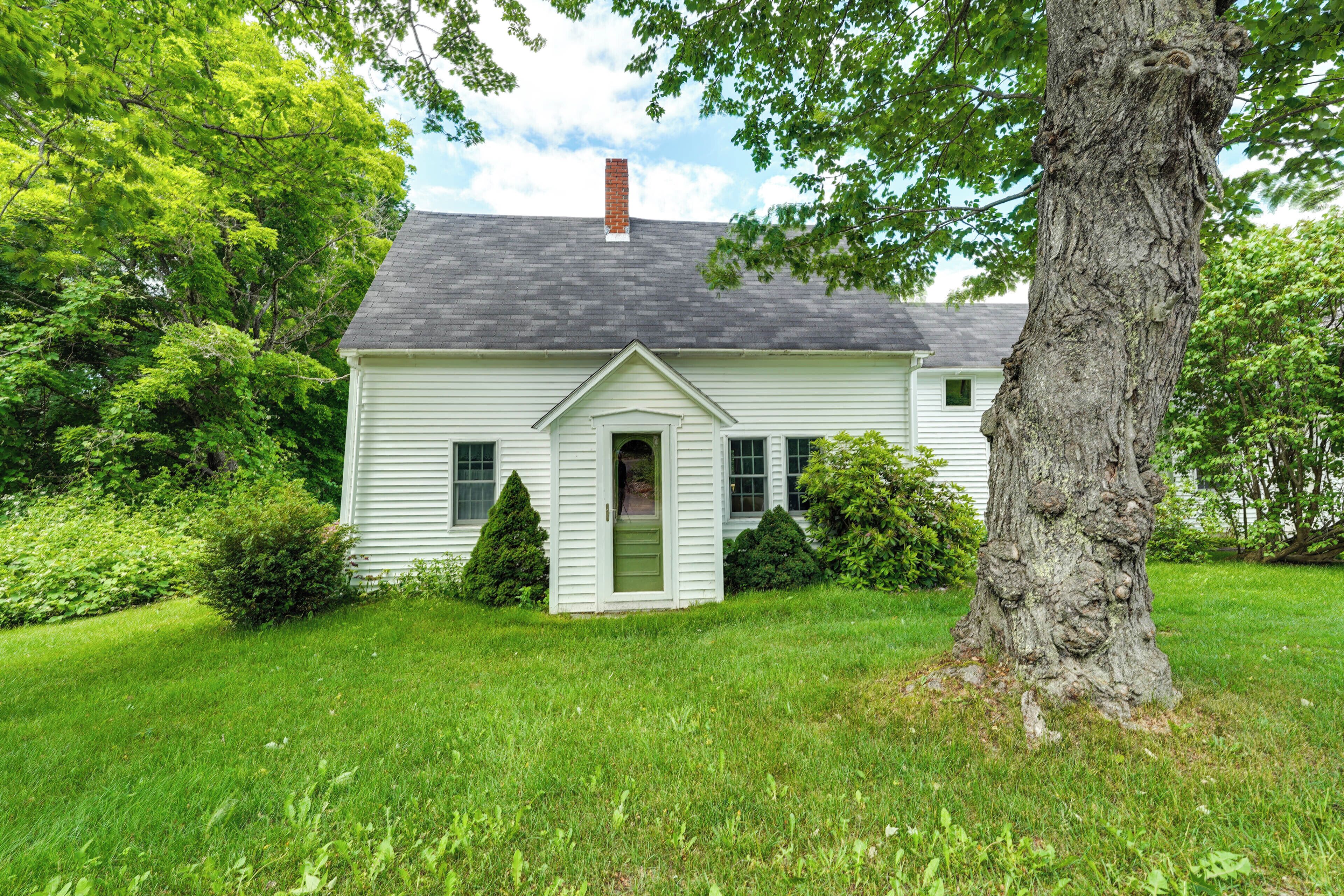 Une maison de plain-pied avec une porte d’entrée, une cheminée et un grand arbre devant.