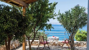 Un patio con una mesa y sillas, vista al mar y un muro de piedra.