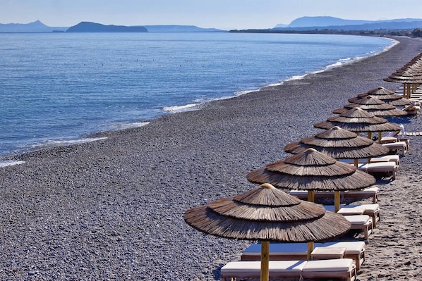 Ein Strand mit Liegestühlen und strohgedeckten Sonnenschirmen.