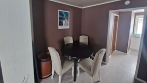 Una habitación con una mesa redonda, cuatro sillas, un cartel en la pared y un cubo de basura.