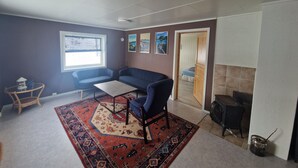 Una sala de estar con sofá, una mesita, alfombra estampada, chimenea y ventana con persianas.