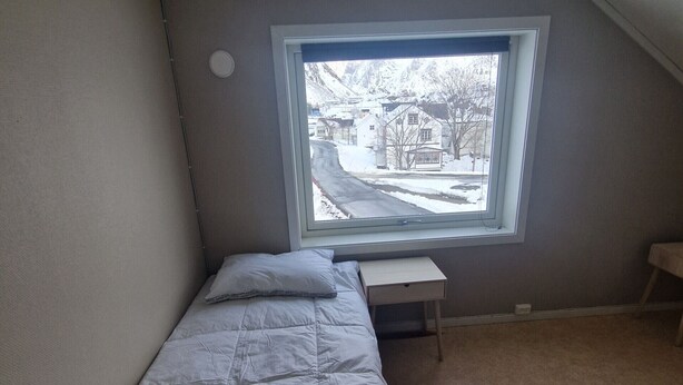 Una habitación pequeña con cama individual y ventana con vista a un paisaje nevado.
