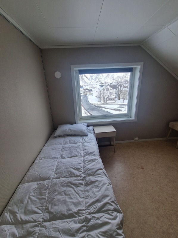 Ein kleines Zimmer mit einem Einzelbett und einem Fenster mit Blick auf eine verschneite Landschaft.