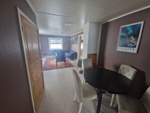 A room with a wooden door, a black table with chairs, a patterned rug, and a framed picture of the Northern Lights on the wall.