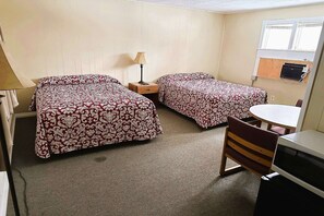 Ein Zimmer mit zwei Betten, einem kleinen Tisch, einem Stuhl und einem Schreibtisch.