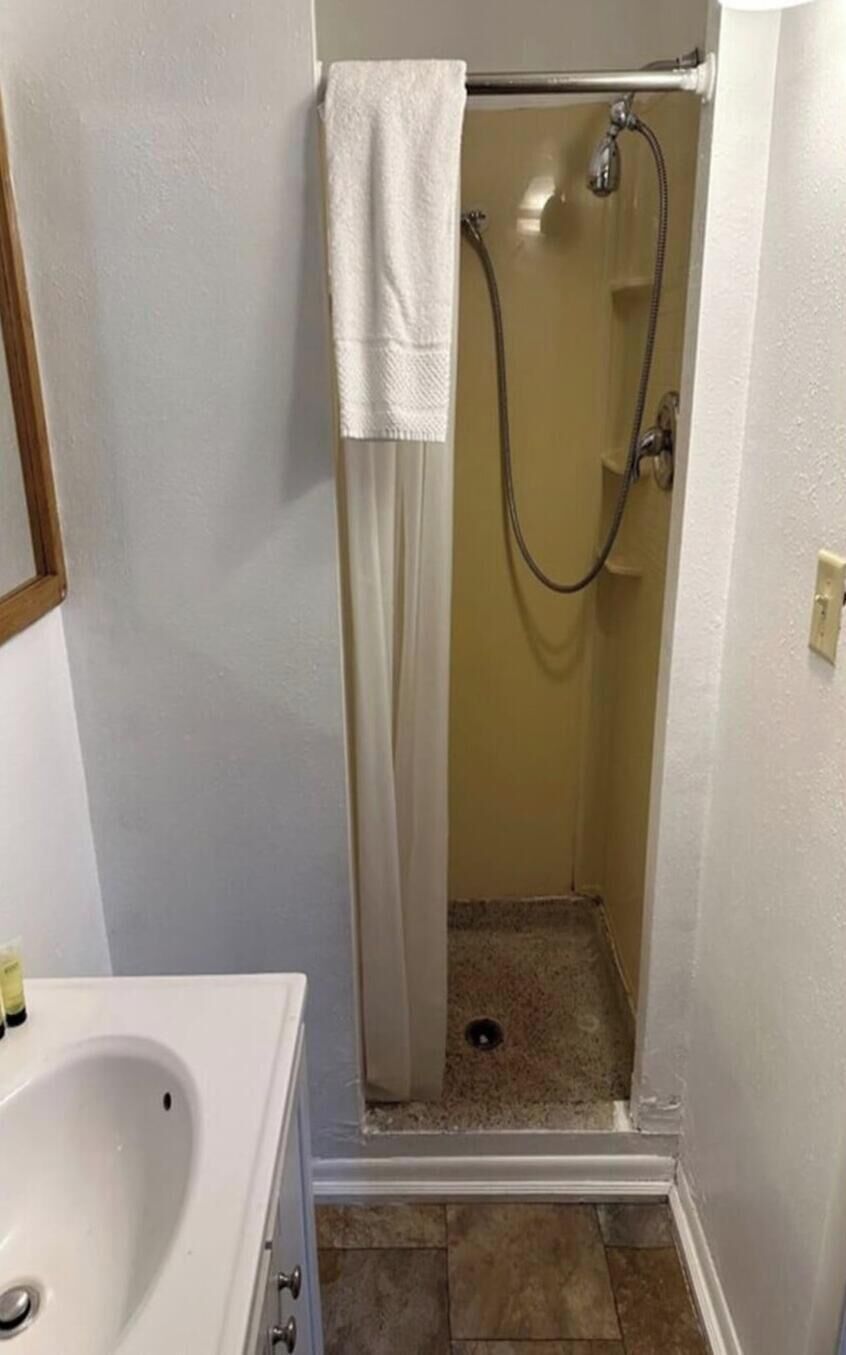 Un baño pequeño con cabina de ducha, lavamanos blanco y piso de baldosas.