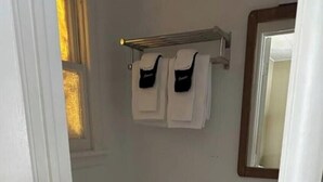 Ett litet badrum med en toalett, ett handfat och en spegel. Ovanför handfatet finns en handduksställare med två handdukar hängande på den.