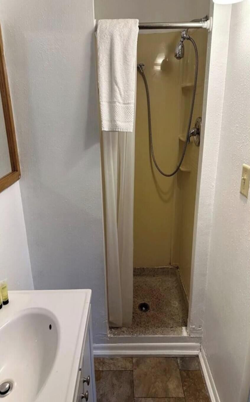 Un baño pequeño con cabina de ducha, lavamanos blanco y piso de baldosas.