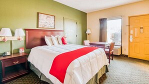 A hotel room with a bed, bedside tables, a desk, a chair, a window with curtains, and a door.