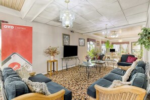 Habitación de hotel con alfombra estampada, sofás oscuros, una mesa de centro de vidrio, televisor y un letrero rojo de OYO Hotels.