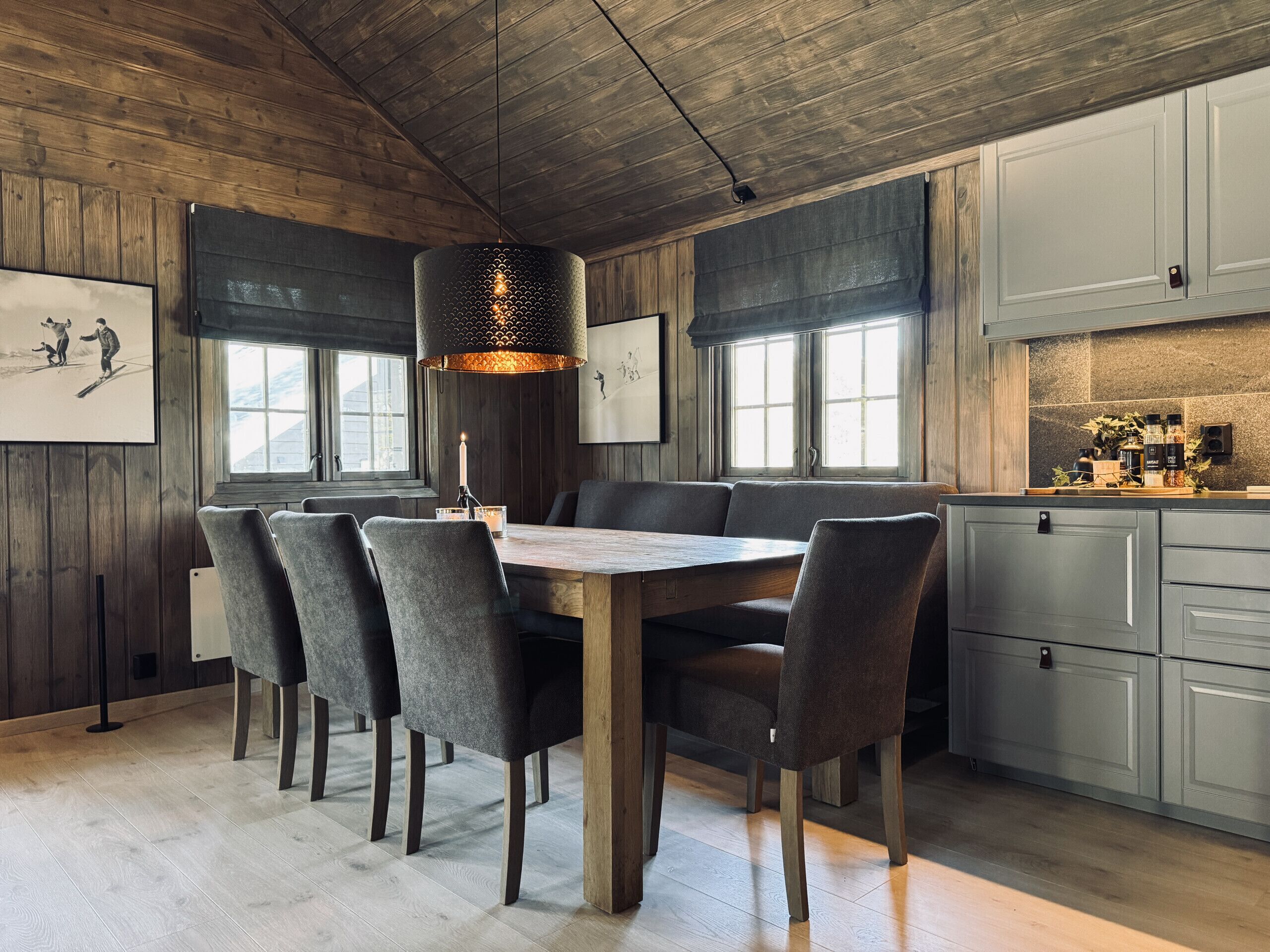 Un comedor con una mesa de madera, sillas tapizadas grises y una lámpara colgante.