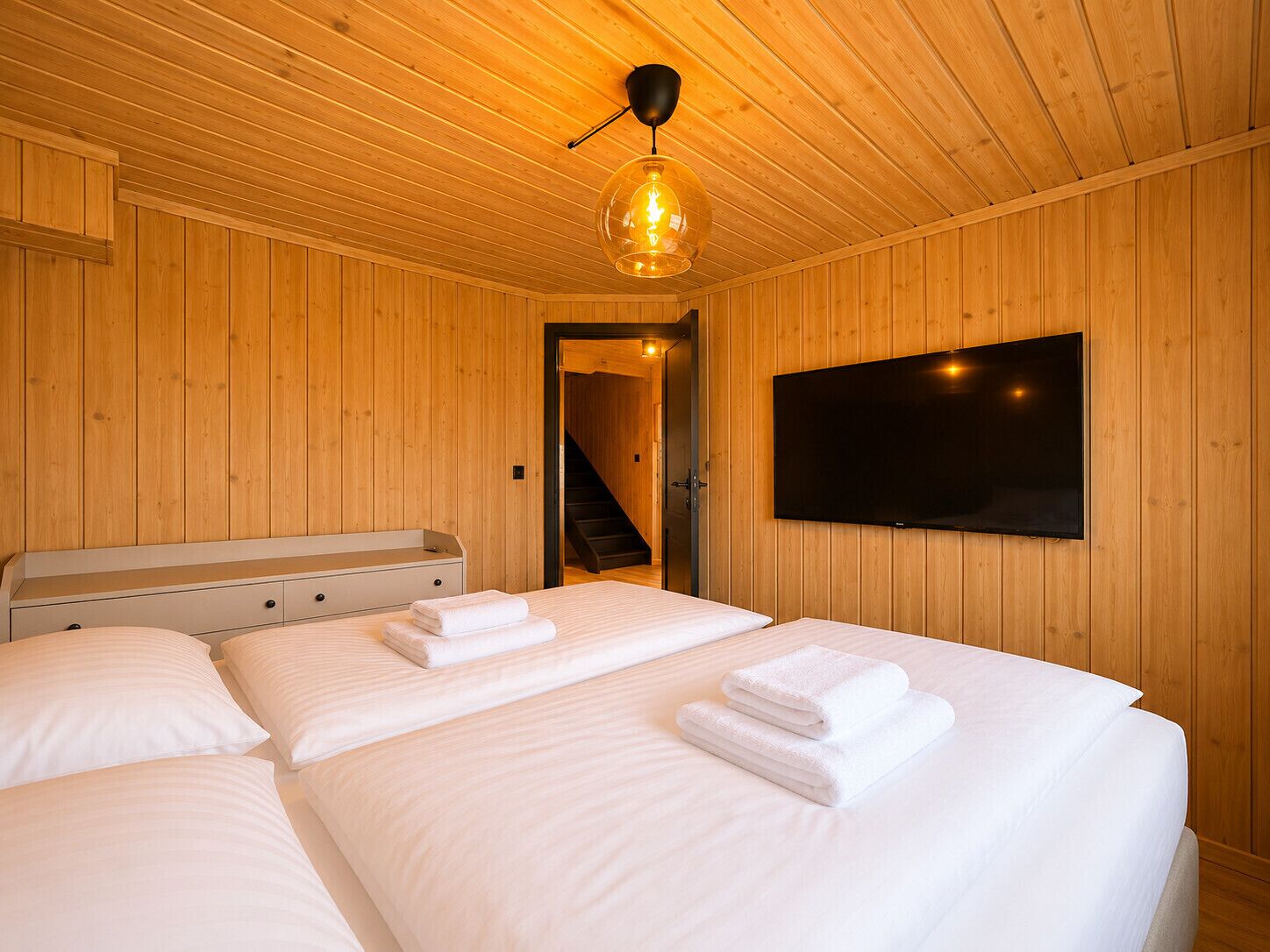 A wooden-paneled room with two beds, a TV, and a staircase.
