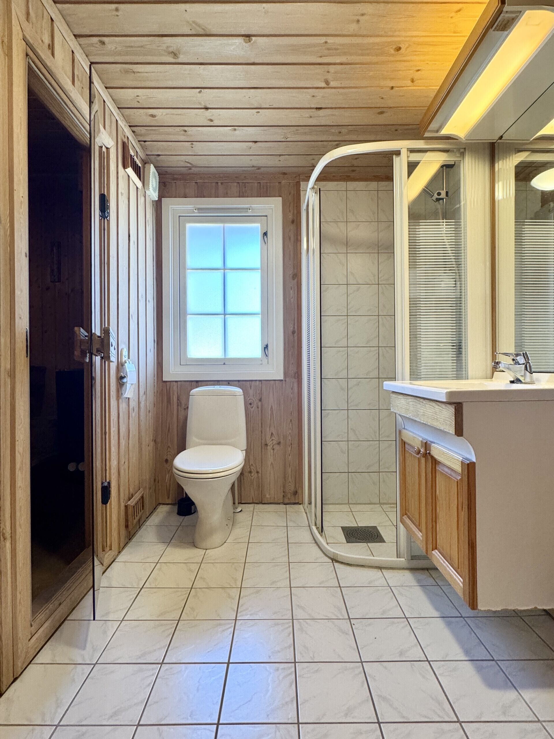A wooden-paneled bathroom with a toilet, shower, and sink.