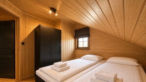 Ein Zimmer mit zwei Betten, Holzwänden, einem dunklen Kleiderschrank und einem Fenster mit Ausblick.