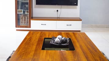 Un salon moderne avec une table basse en bois, un téléviseur à écran plat fixé sur un meuble de télévision blanc, et un meuble vitré contenant des objets décoratifs.