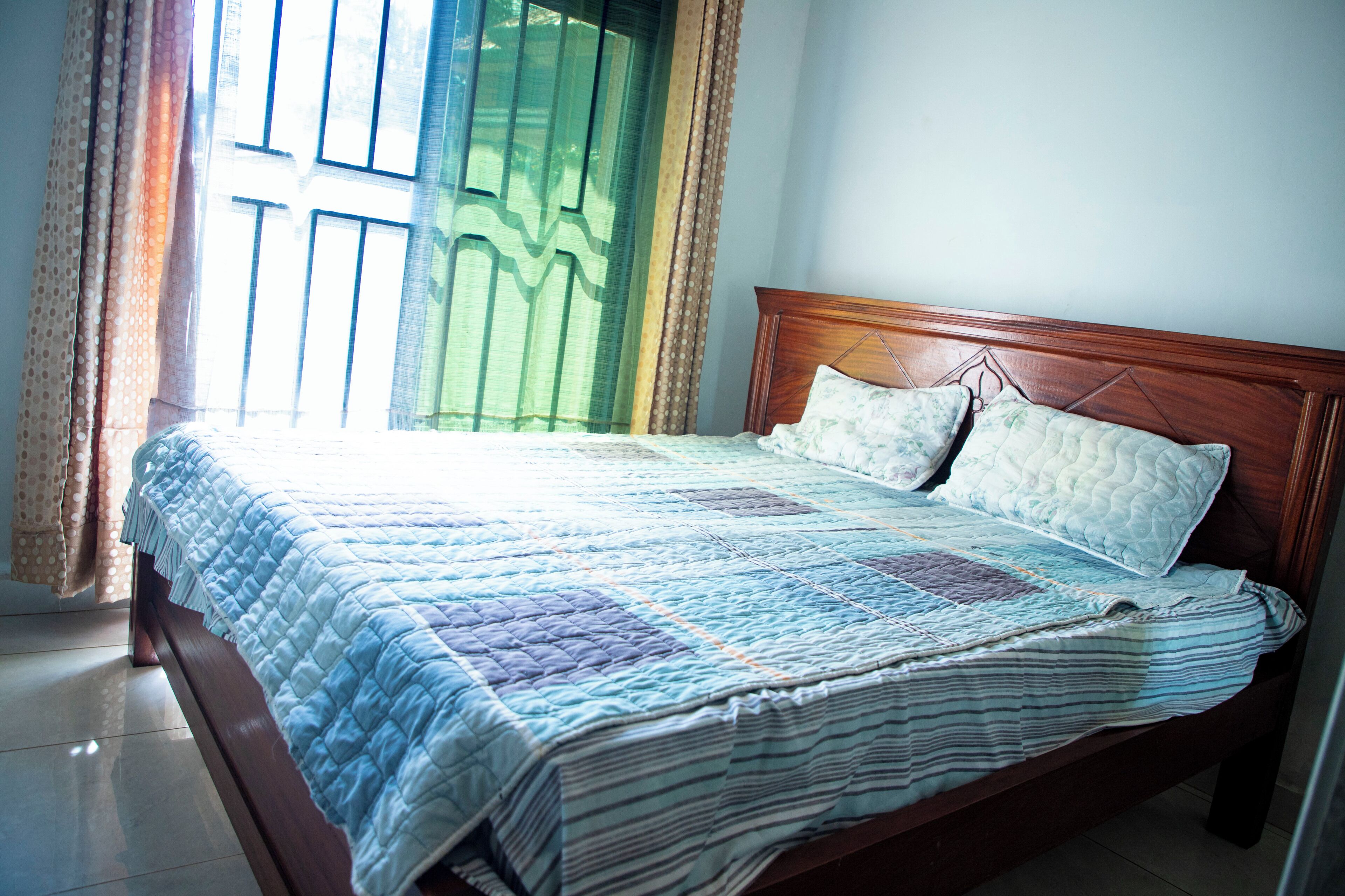 A bed with a quilt, a wooden headboard, and curtains.