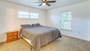 Un dormitorio con cama, mesita de noche, ventilador de techo y dos ventanas.