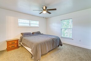Ein Schlafzimmer mit einem Bett, einem Nachttisch, einem Deckenventilator und zwei Fenstern.
