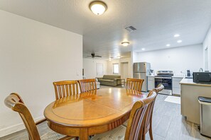 Ein Essbereich mit Holztisch und Stühlen, einem Deckenventilator, Einbauleuchten, einer Küchenzeile mit Geräten und einem Sofa im Hintergrund.