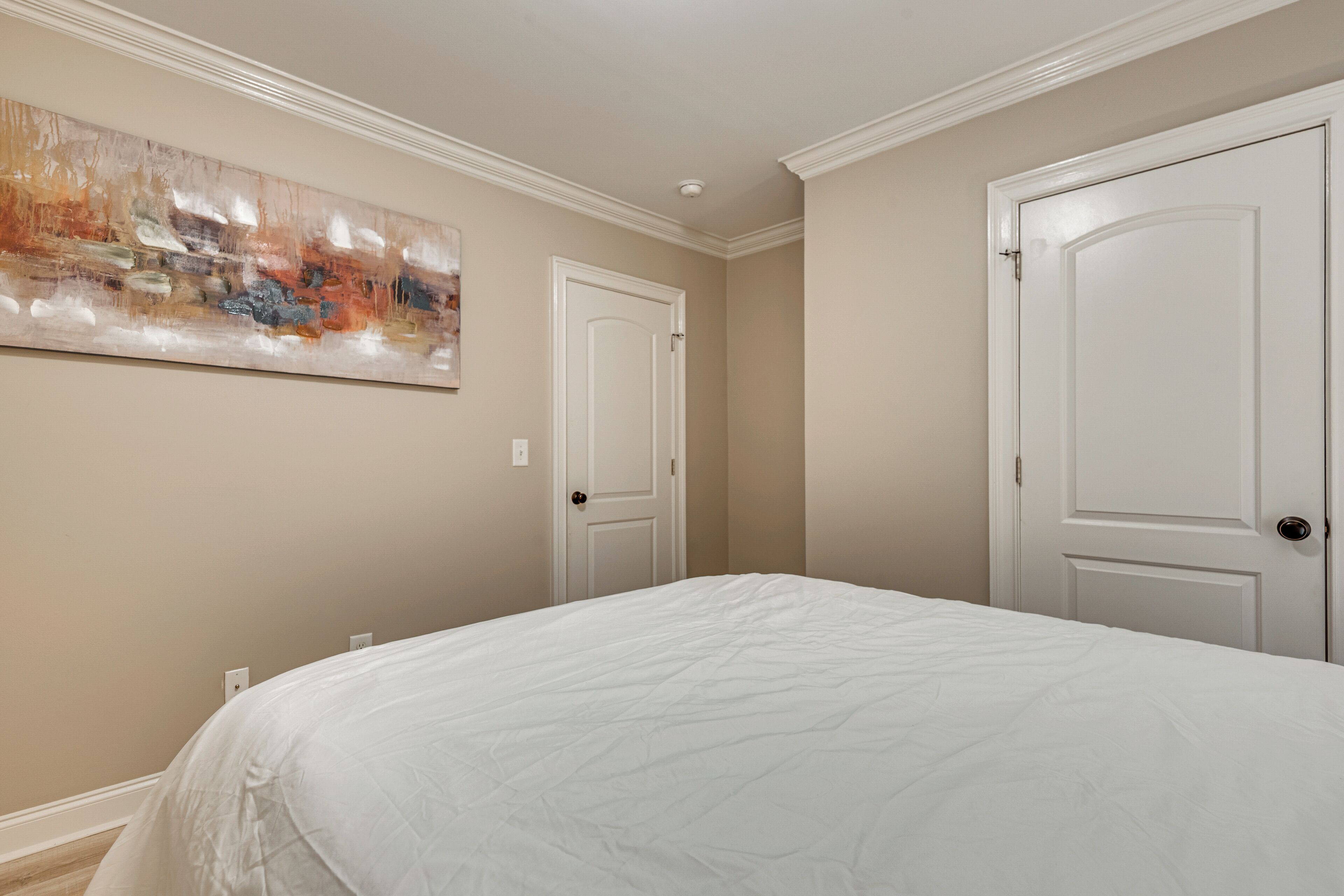 Ein Schlafzimmer mit einem großen Bett, zwei weißen Türen und einem Bild an der Wand.