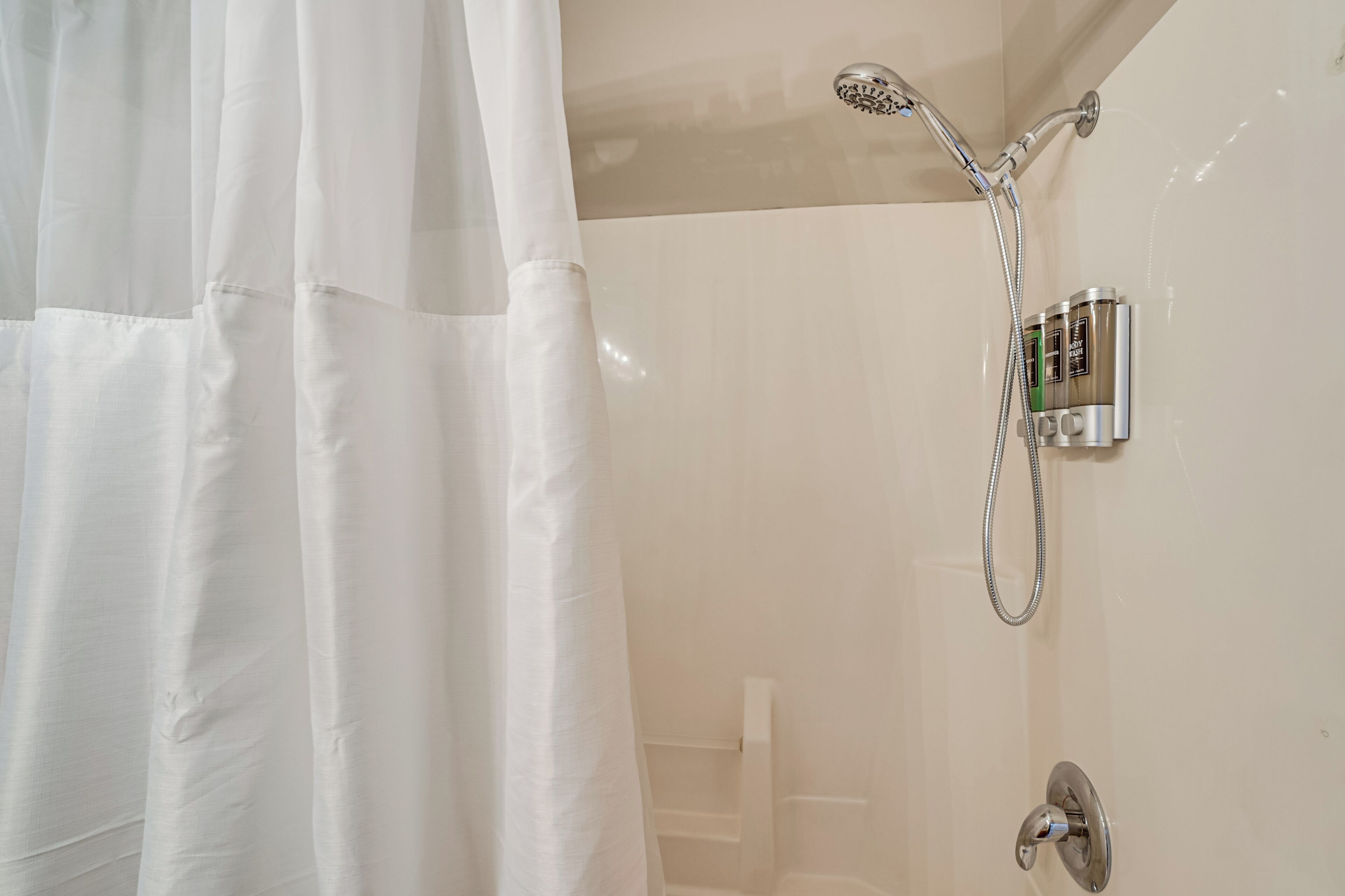 Eine Dusche mit Handbrause, Bedienfeld an der Wand und einer Duschkabinentür.