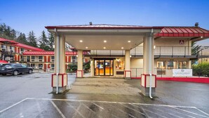 En hotellentrén med en överbyggd gångväg, en receptionsdisk och en parkeringsplats.