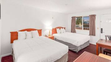 A hotel room with two beds, a desk, a chair, a lamp, and a window with curtains.