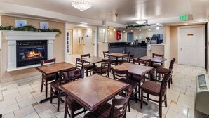 Un hall d’hôtel doté d’une cheminée, de plusieurs tables et chaises, d’un coin cuisine et d’un panneau indiquant la sortie.