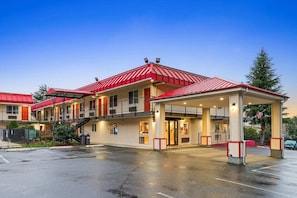 Um hotel de vários andares com telhado vermelho, entrada coberta e estacionamento.