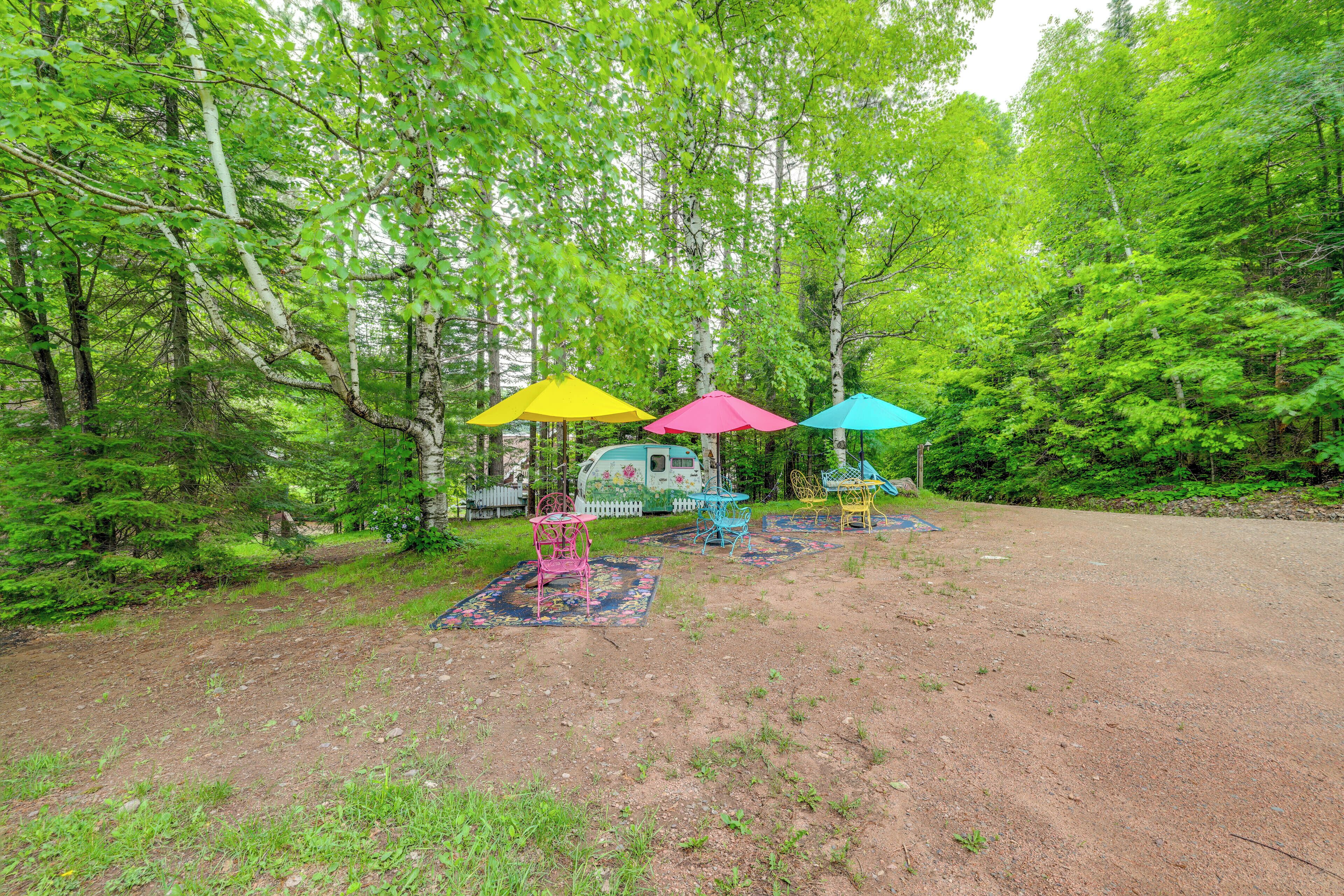 Un terrain de camping agrémenté de parasols et de chaises aux couleurs vives, entouré d’une forêt dense.