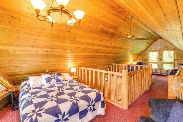 A wooden cabin bedroom with a bed, a ceiling fan, and a view of the outdoors.