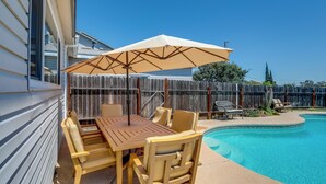 Ein Garten mit Holztisch und -stühlen, einem Pool und einem Holzzaun.