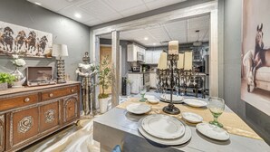 A dining area with a table set for four, a wooden cabinet with decorative items, and a painting of horses on the wall. - 5 Min to Broken Bow Lake! Stylish Retreat w/ Deck (Broken Bow)