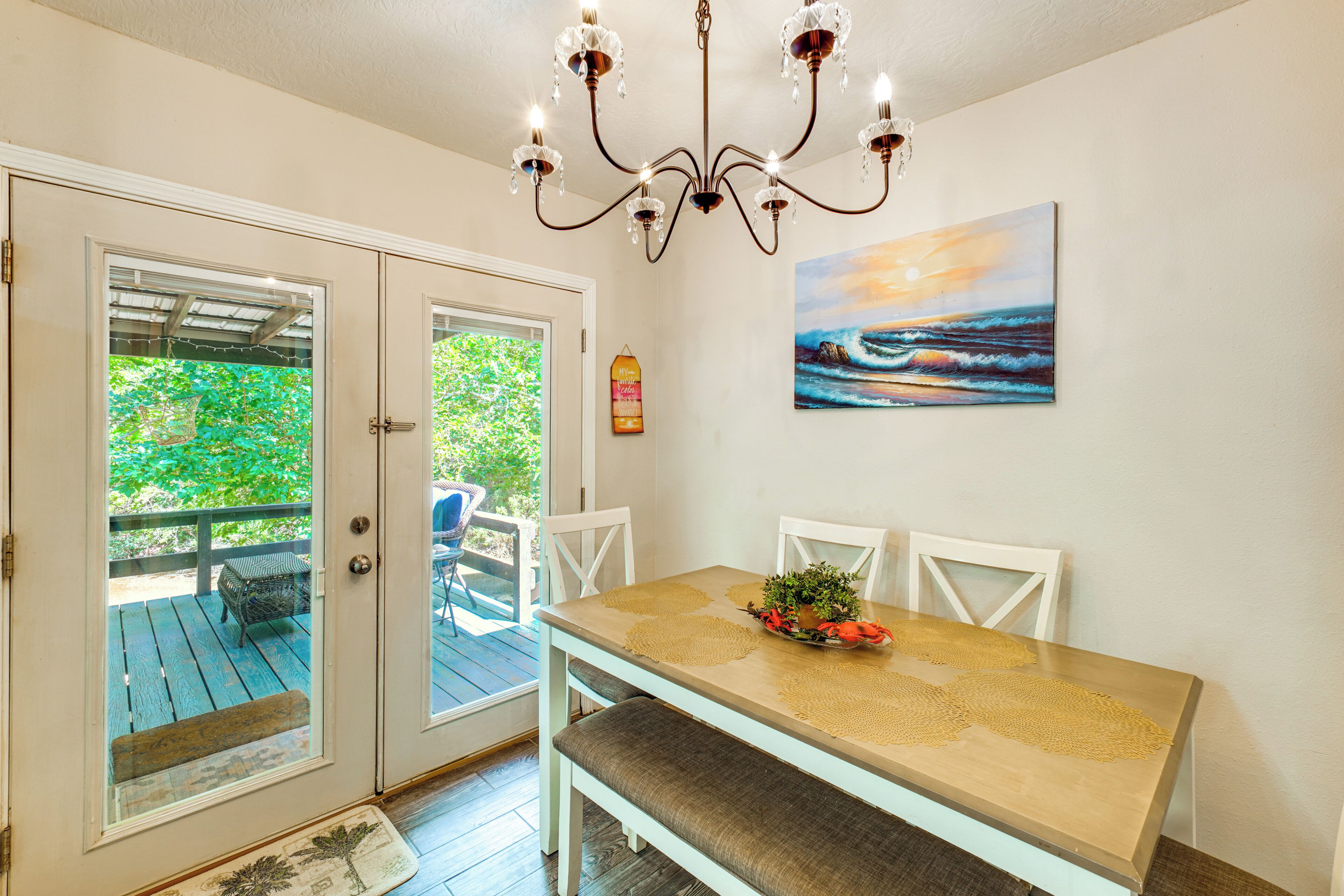 Un espace repas comprenant une table, des chaises, un lustre, un tableau et une vue à travers une porte vitrée.
