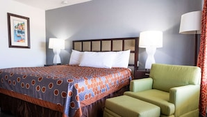 Ein Hotelzimmer mit einem großen Bett, zwei Nachttischlampen, einem grünen Sessel und einem kleinen Hocker.