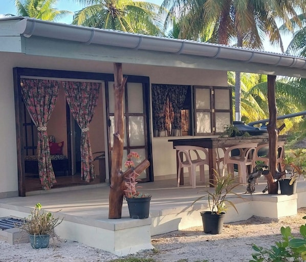 A covered outdoor area with a table and chairs, potted plants, and a wooden structure.